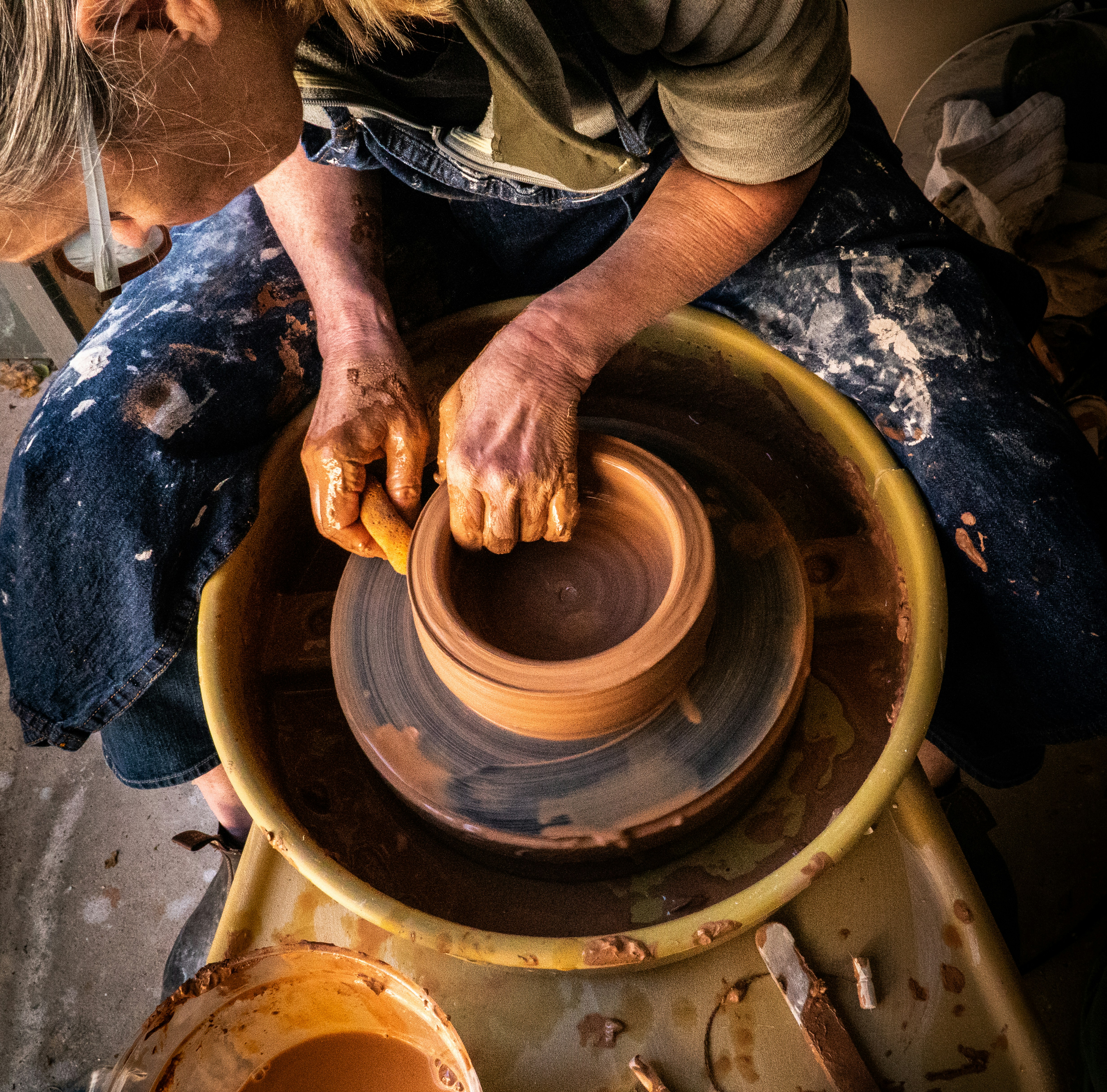 A person shaping a clay pot on a pottery wheel